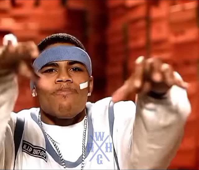 A man wearing a blue headband and white sweatshirt gesturing towards the camera.