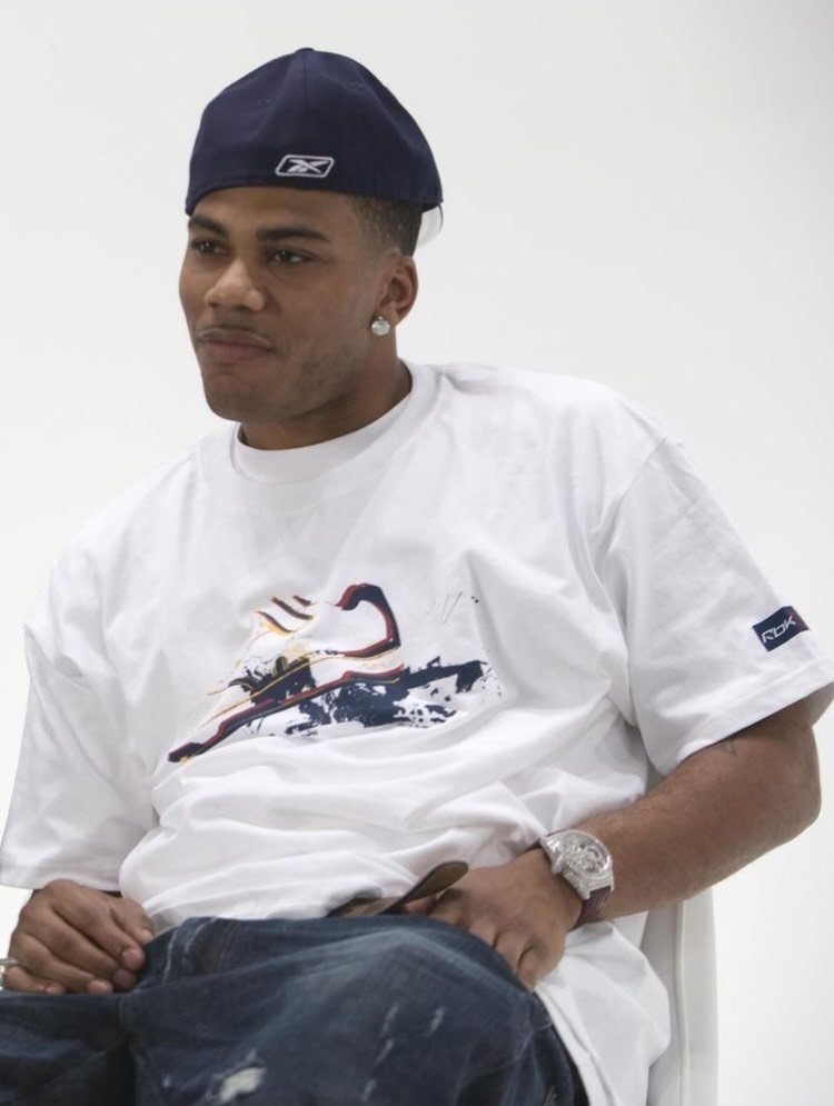 Man in oversized white graphic t-shirt, baggy jeans, and a navy blue baseball cap.