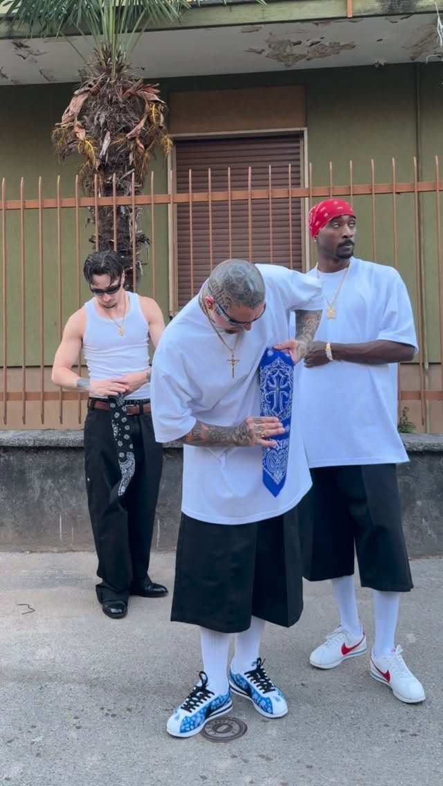 Three men wearing oversized white shirts and baggy black shorts standing outdoors.