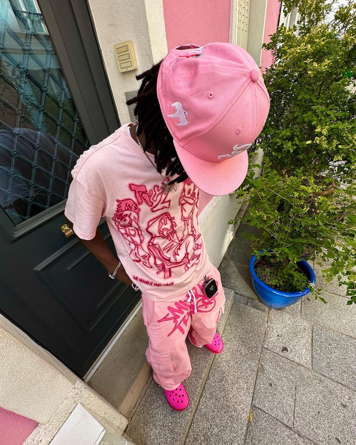 A person dressed in an all-pink outfit including a cap, t-shirt, pants, and Crocs.