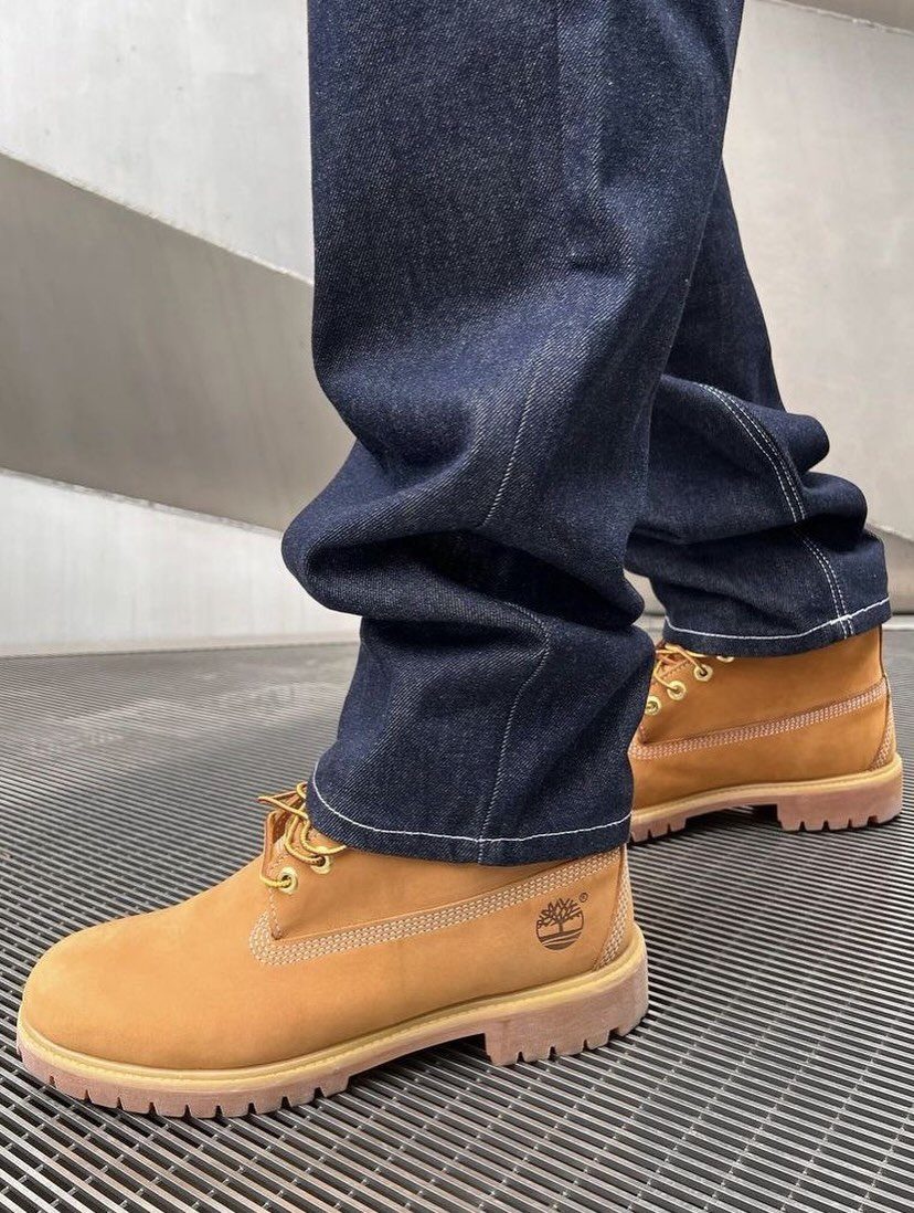 Person wearing baggy dark blue denim jeans and tan work boots on a metal grate.