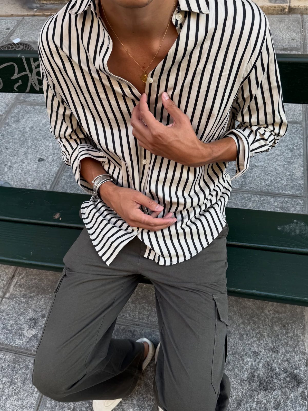 A person wearing a striped shirt and olive green cargo pants sitting on a bench.