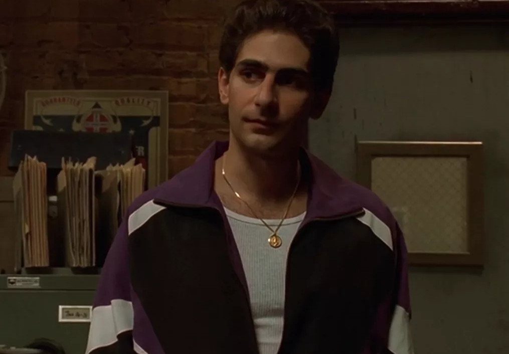 A young man wearing a purple and black color-blocked tracksuit jacket and a gold necklace.