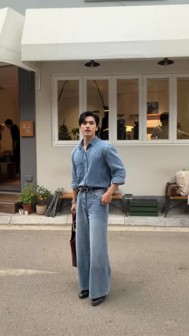 A man posing in a denim shirt and wide-leg denim jeans outdoors.
