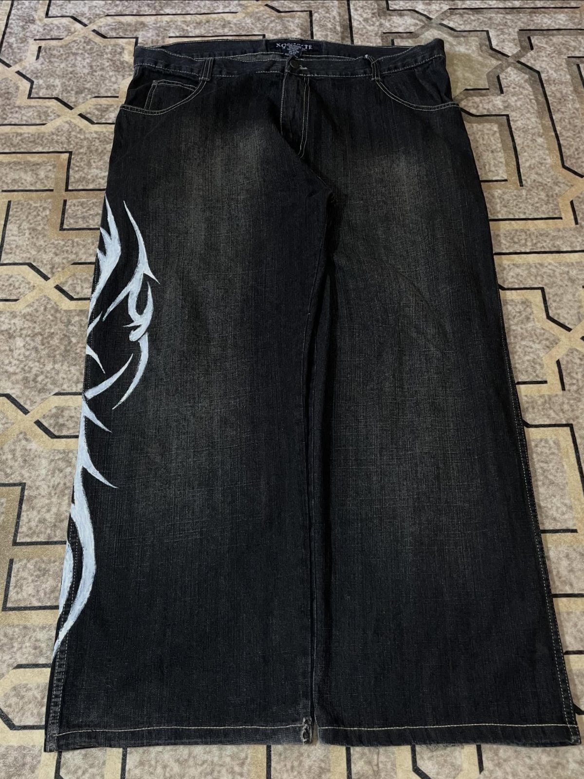 Dark wash wide-leg denim jeans with a white flame graphic design laid on a tiled floor.