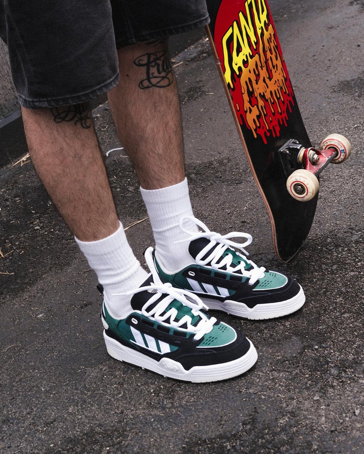 Person wearing black and teal retro sneakers with white crew socks standing near a skateboard.