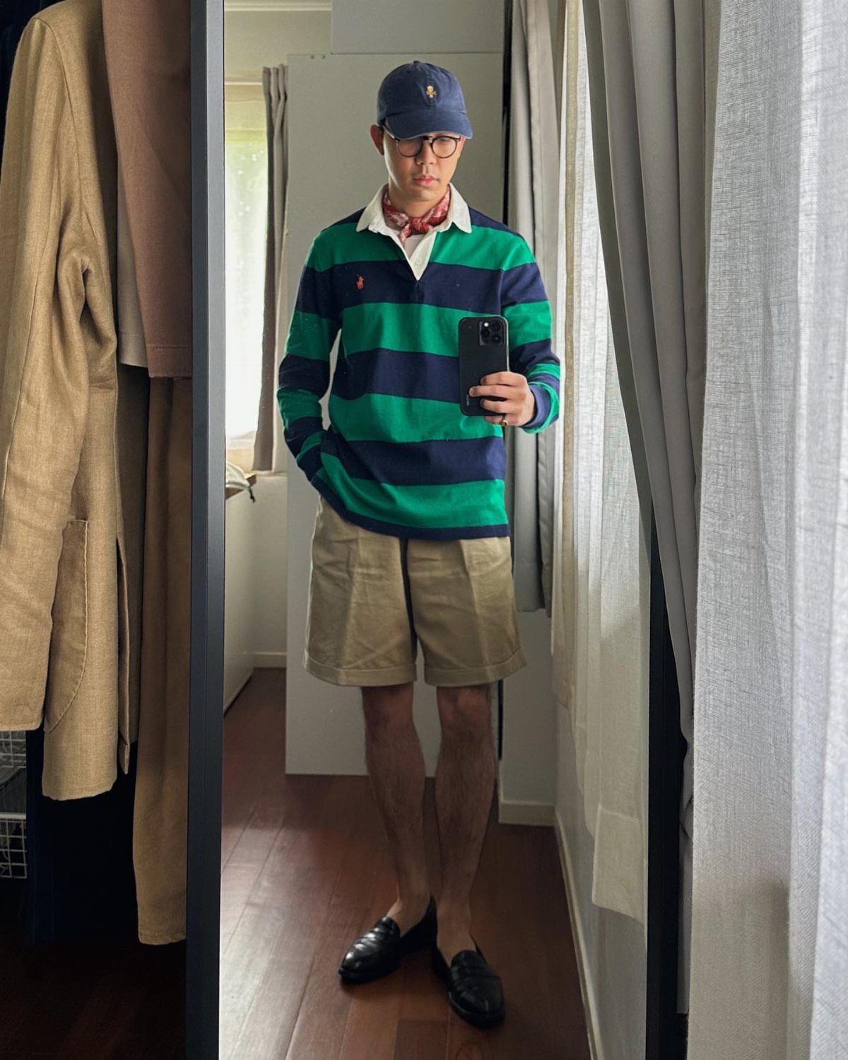 A man in a green and navy striped rugby shirt, khaki shorts, and a blue cap.