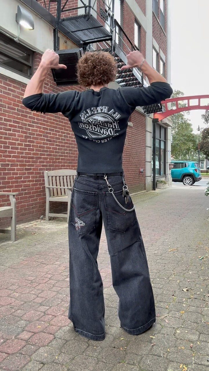 A person wearing baggy black jeans and a tight graphic shirt with a wallet chain.