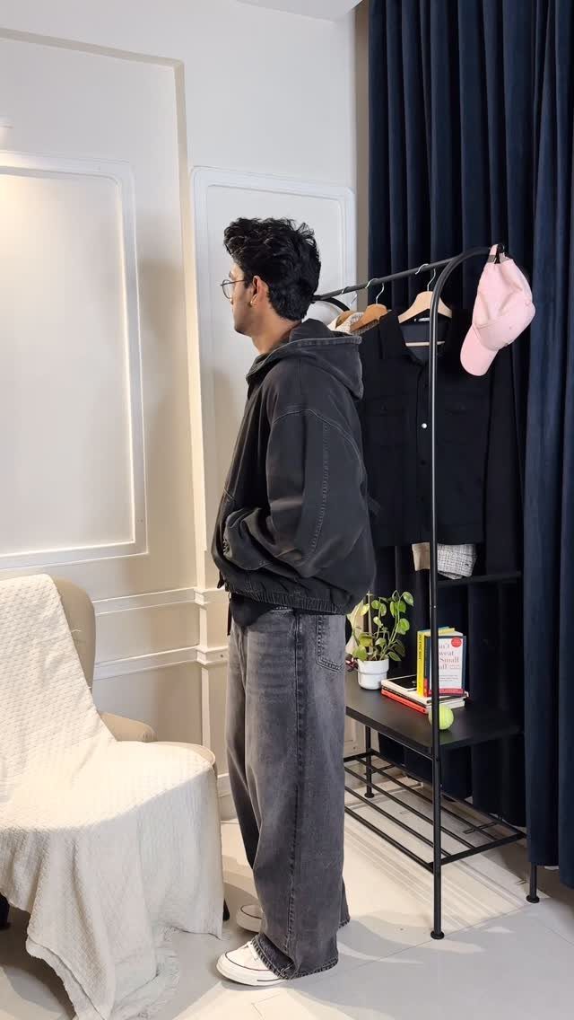 Man in a black hoodie and baggy grey jeans standing next to a clothing rack.