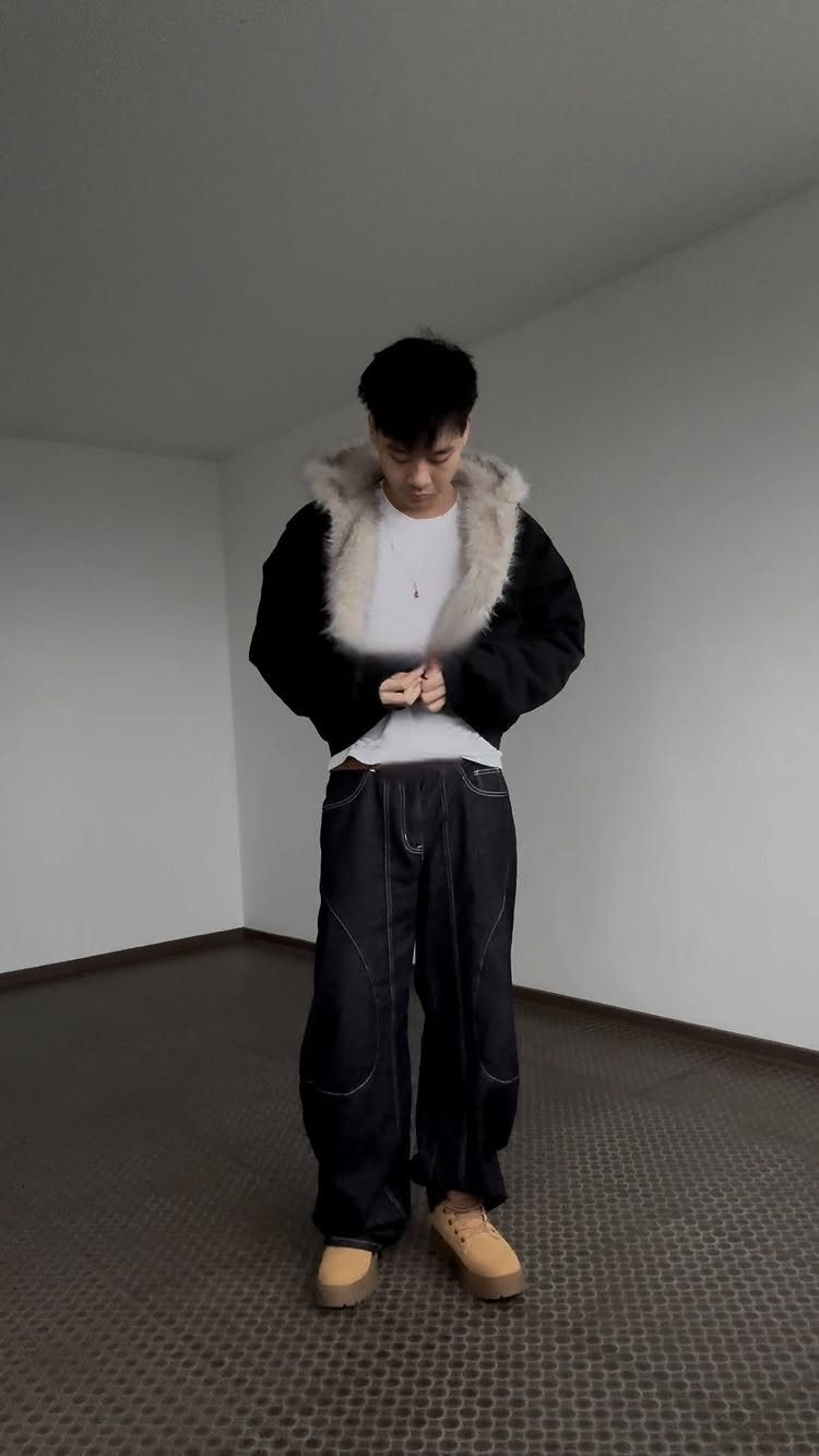 Man wearing a black fur-trimmed jacket, white shirt, baggy dark pants, and tan shoes.