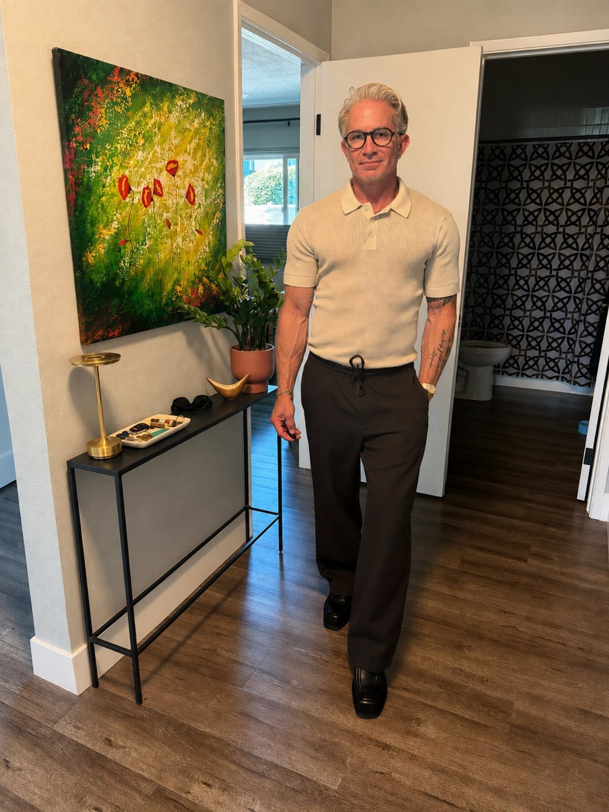 A man in a beige polo shirt and dark trousers posing in a hallway.