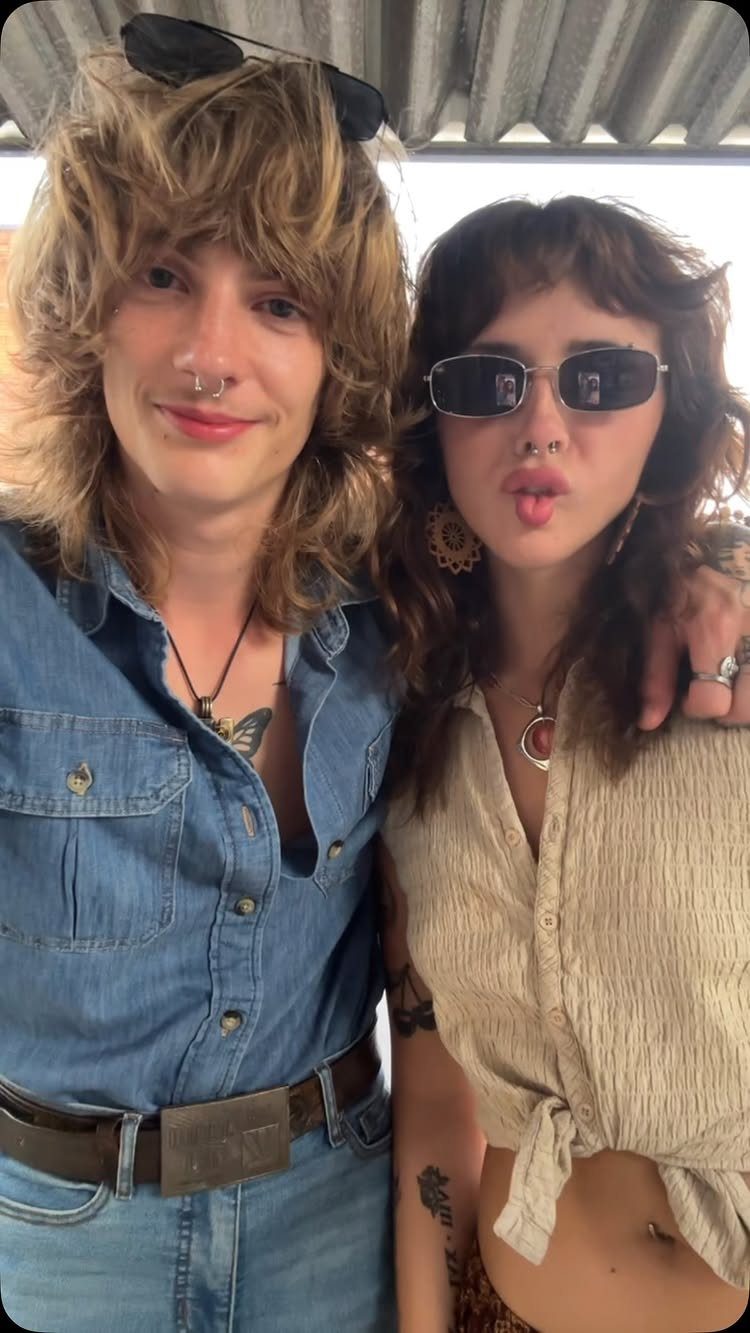 Two people with shaggy hair posing, one wearing a blue denim shirt and jeans.