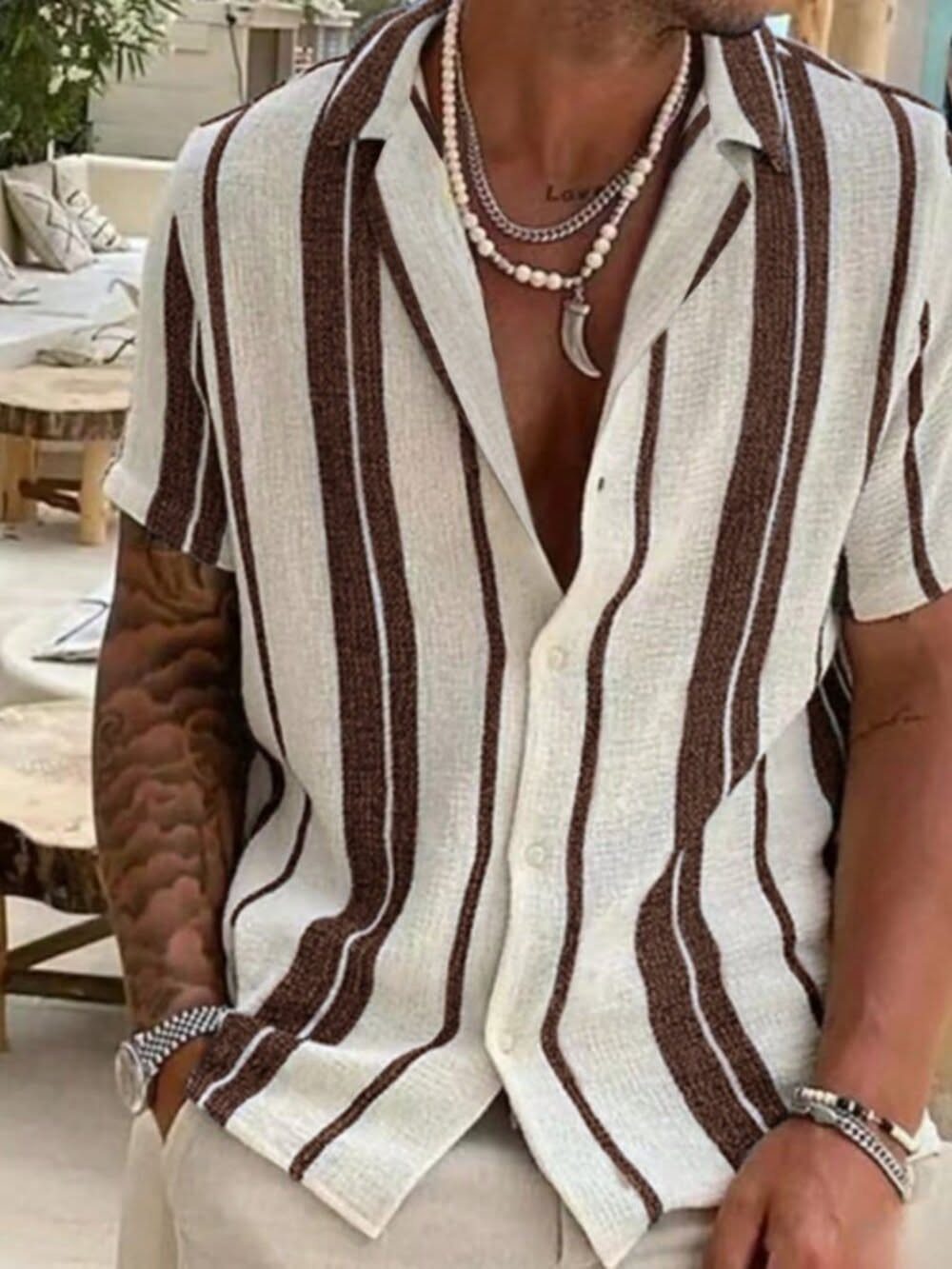 A man wearing a striped linen short-sleeved shirt and layered necklaces.