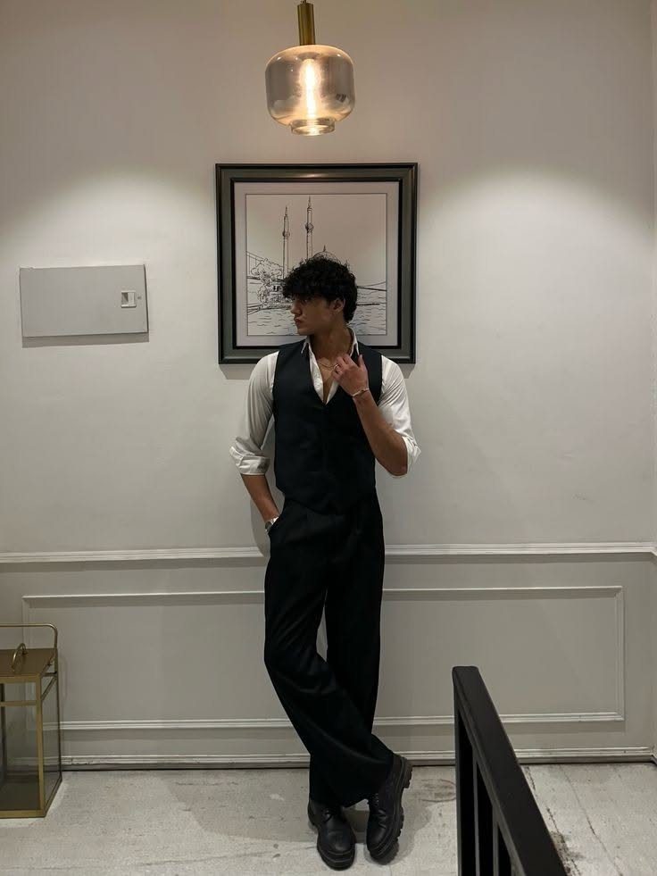 A man wearing a black waistcoat over a white shirt and black trousers standing indoors.