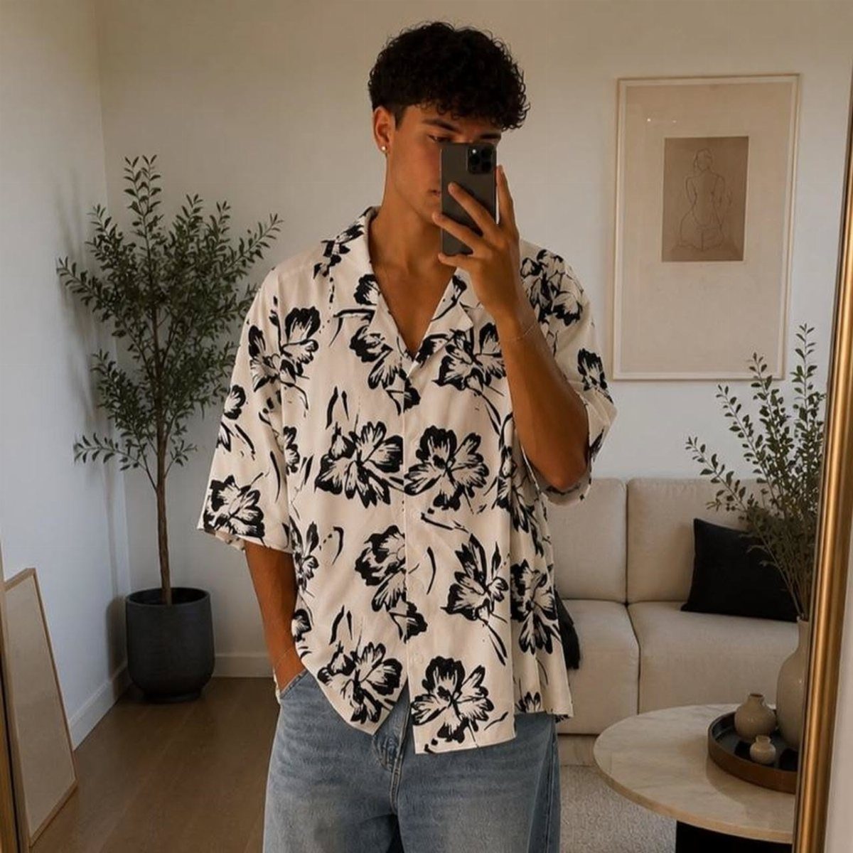 A man in a white shirt with black floral patterns posing for a mirror selfie.