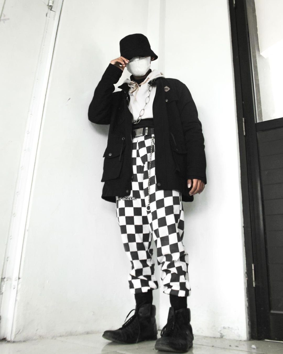 A person wearing a black jacket, white top, and black and white checkered trousers.