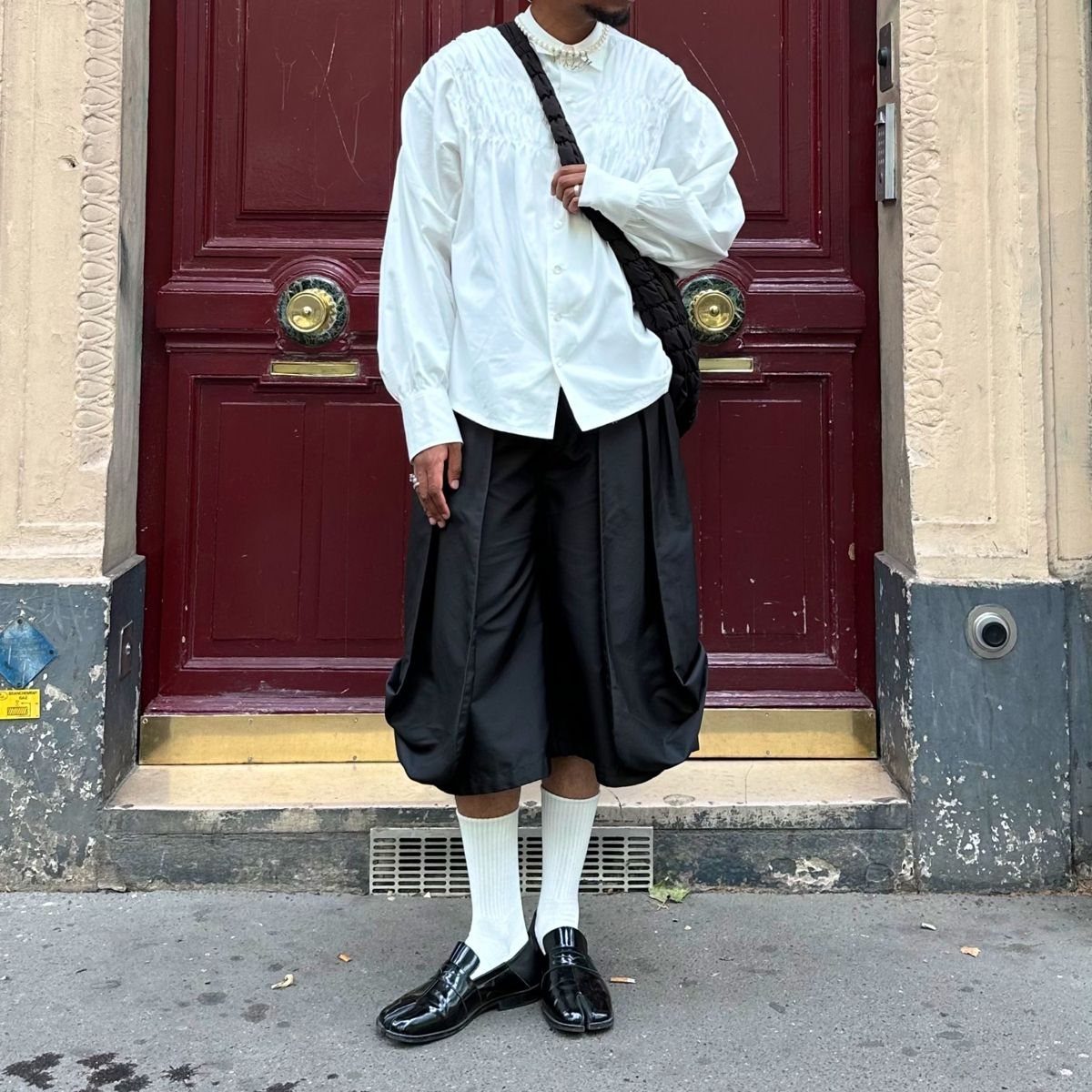 A person wearing a white shirt, black shorts, white socks, and black loafers standing outdoors.