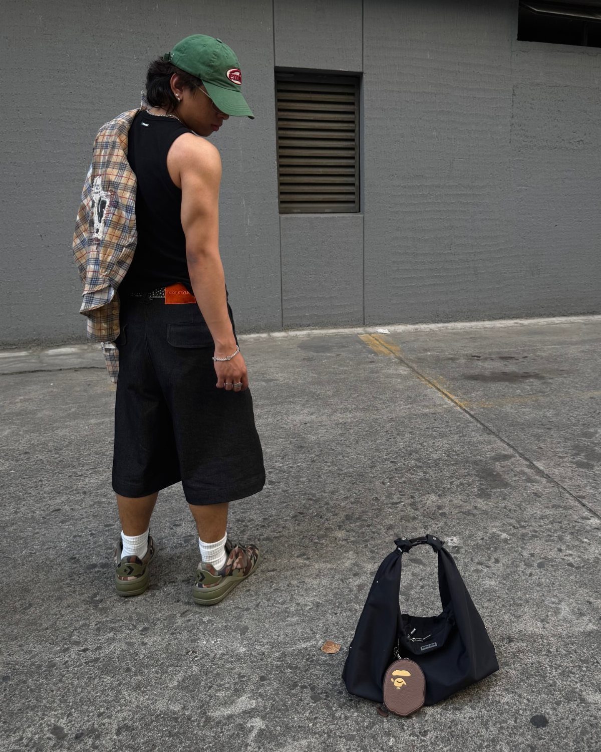 A person wearing a black muscle tee and black shorts standing on a sidewalk.