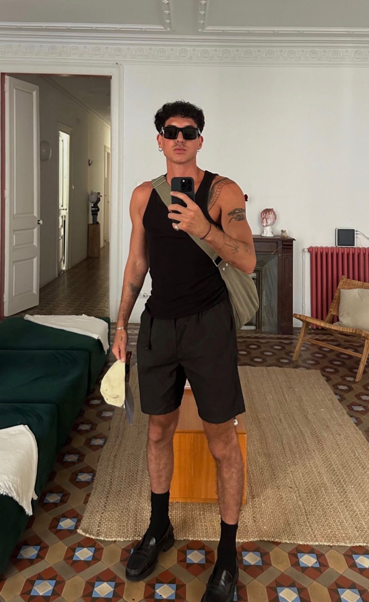 Man in black tank top and dark shorts posing for a mirror selfie indoors.