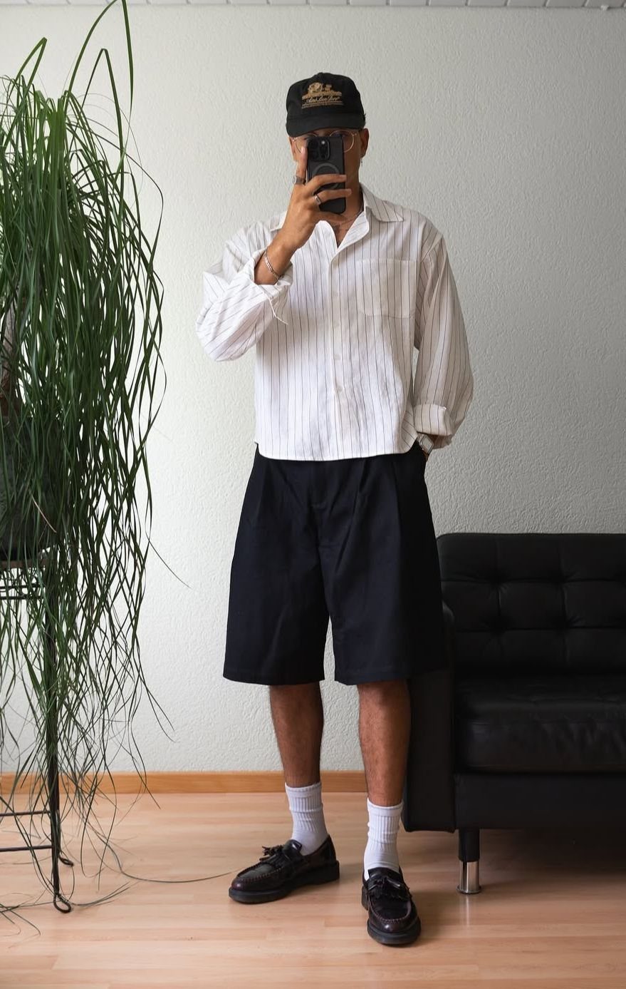 Man in a white striped shirt and black shorts posing for a mirror selfie.