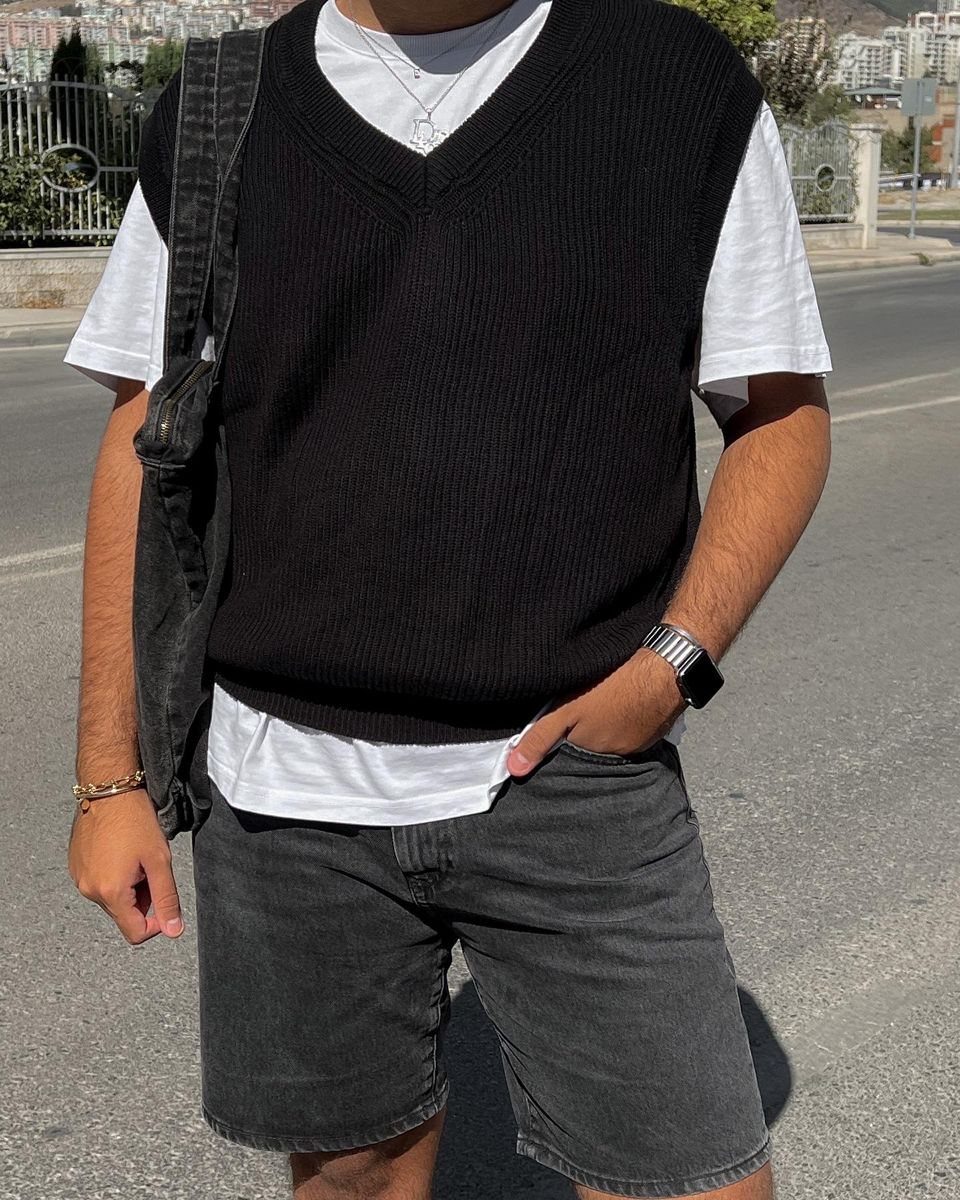 A person wearing a black sweater vest over a white t-shirt and dark shorts.