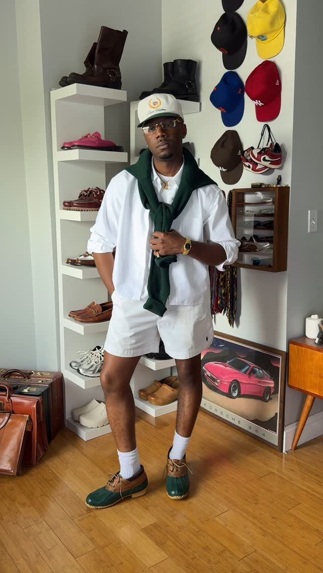 A man wearing white chino shorts, a white shirt, and green boat shoes posing indoors.