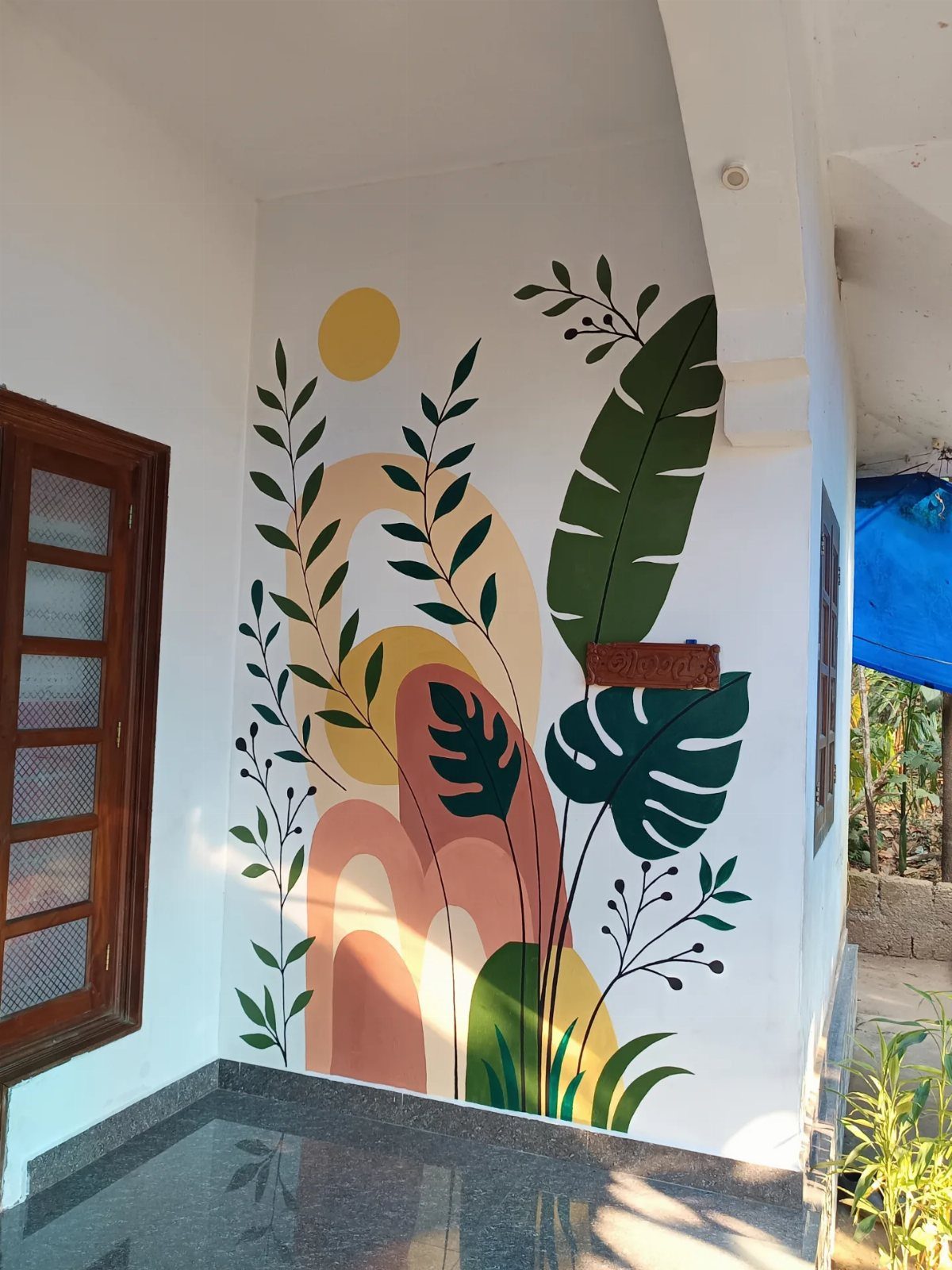 Botanical wall mural with leaves and sun in terracotta, green, and yellow tones.