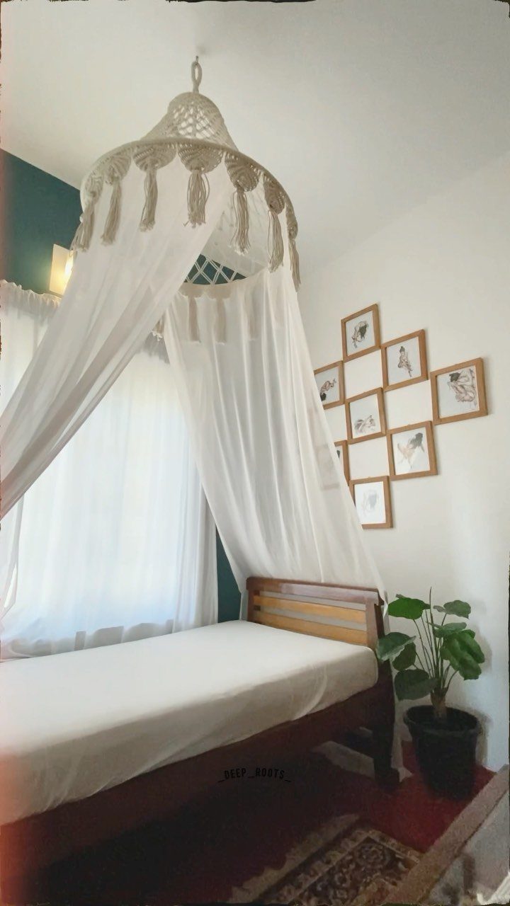 A white fabric canopy with macrame tassels hanging over a wooden bed in a room.
