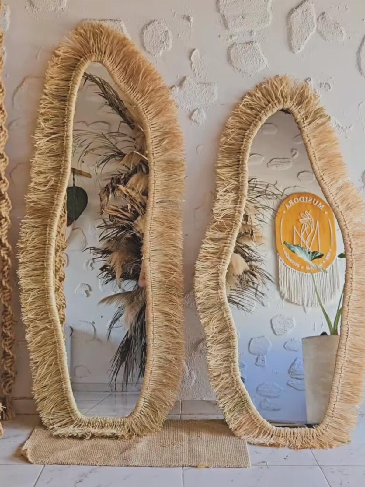 Two oval mirrors with thick, shaggy natural fiber fringe leaning against a white textured wall.