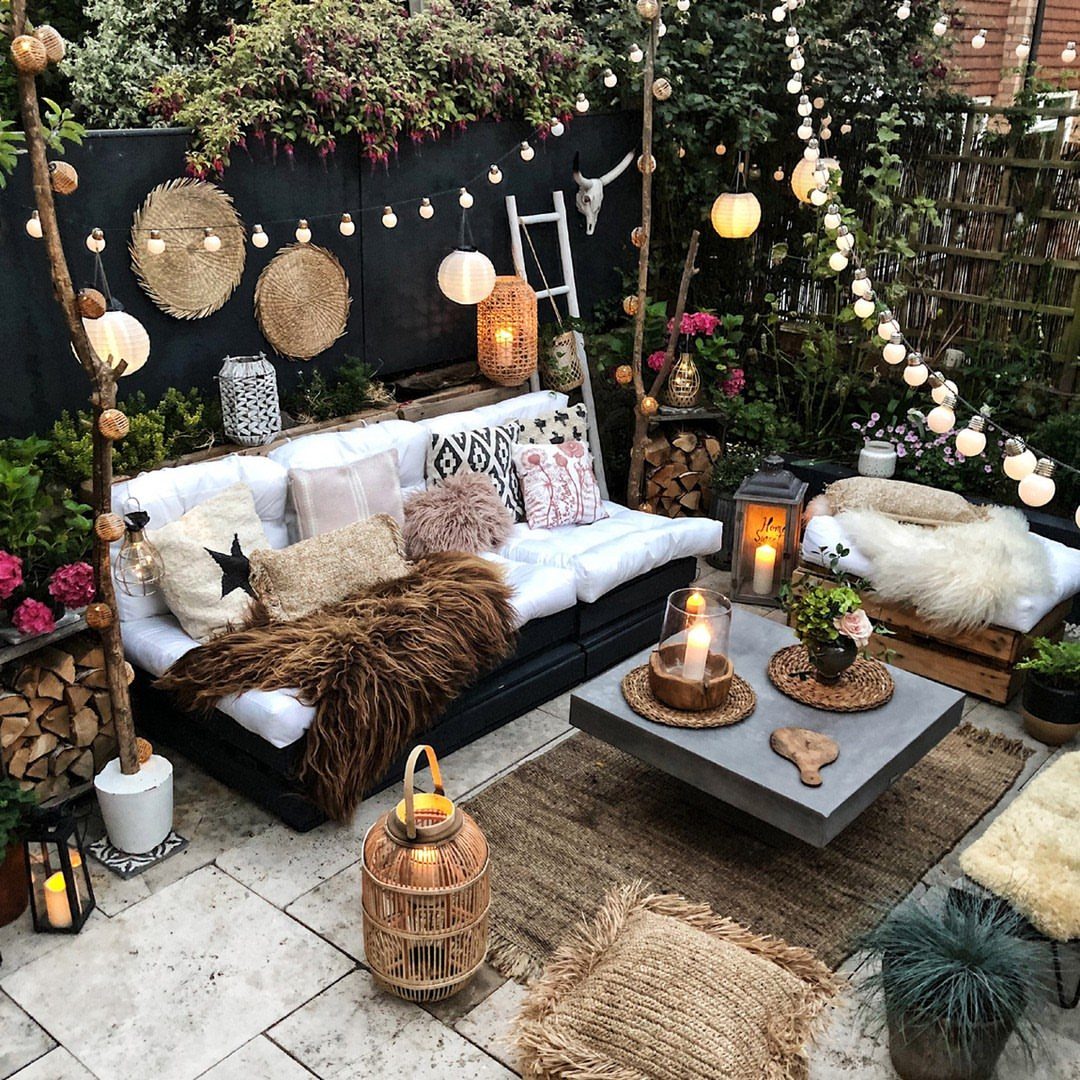 A cozy outdoor patio with a white sofa, textured pillows, and a jute rug on stone tiles.