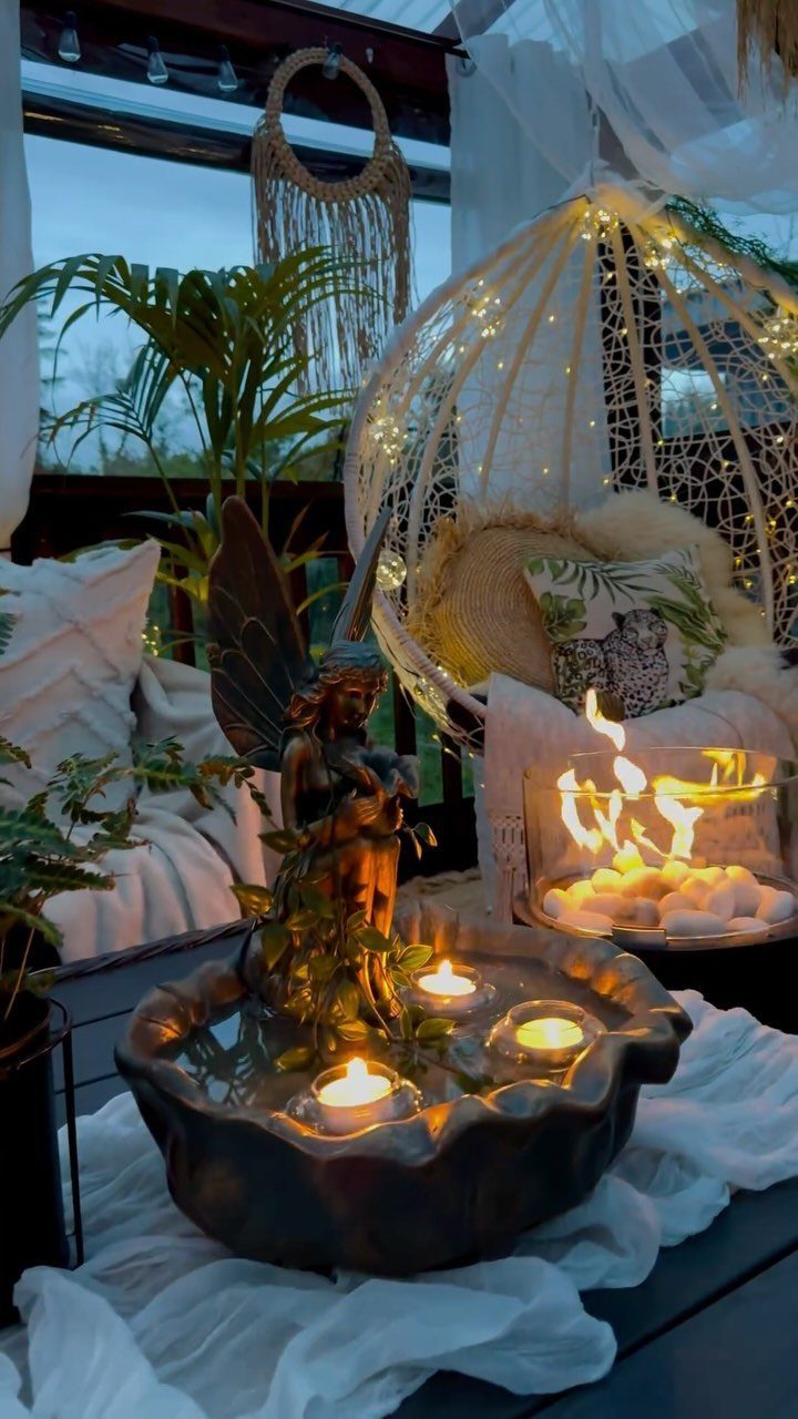 Hanging egg chair with fairy lights surrounded by plants and glowing candles on a patio.