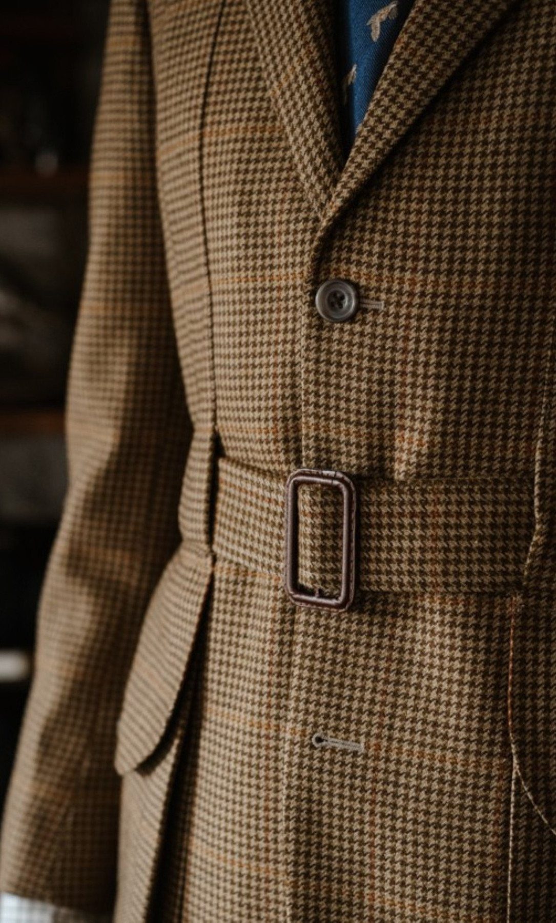 A close-up view of a brown houndstooth patterned wool coat with a belted waist.