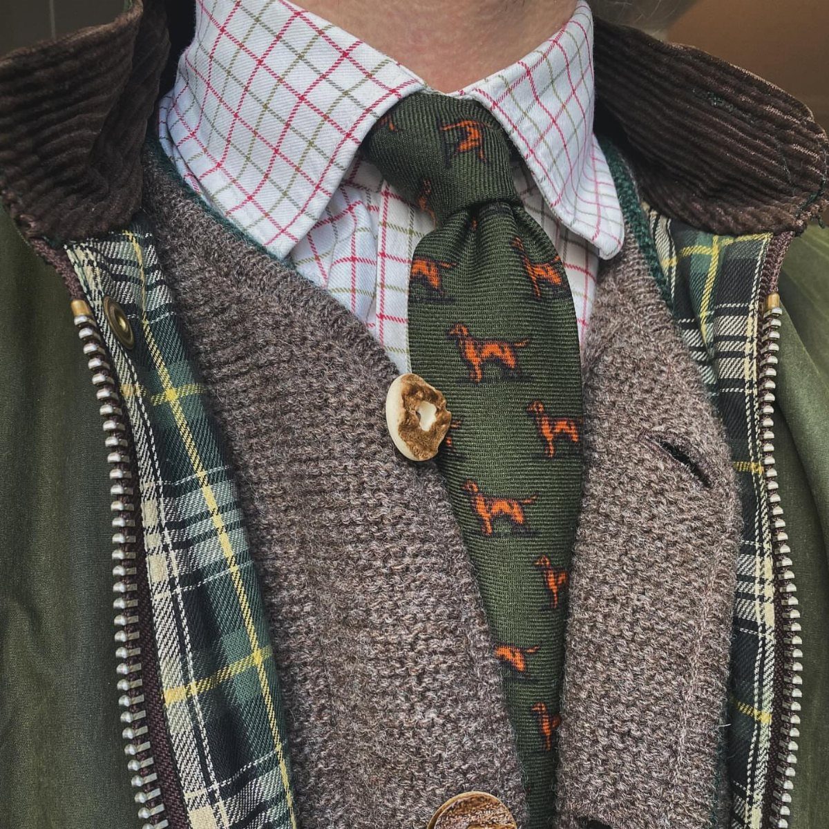 A man wearing a white Tattersall checkered shirt, a dachshund patterned tie, and a brown waistcoat.