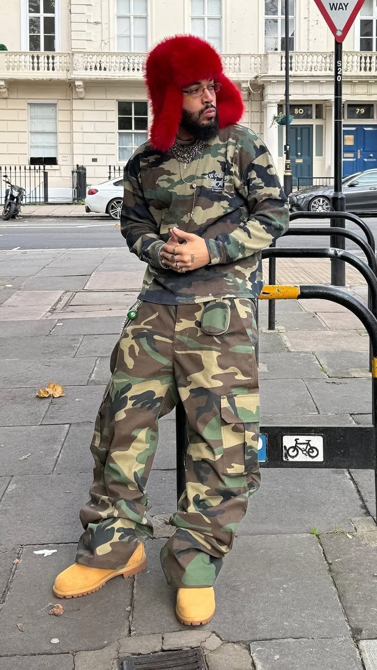 Man in camouflage shirt and cargo pants posing on a city sidewalk wearing tan boots.