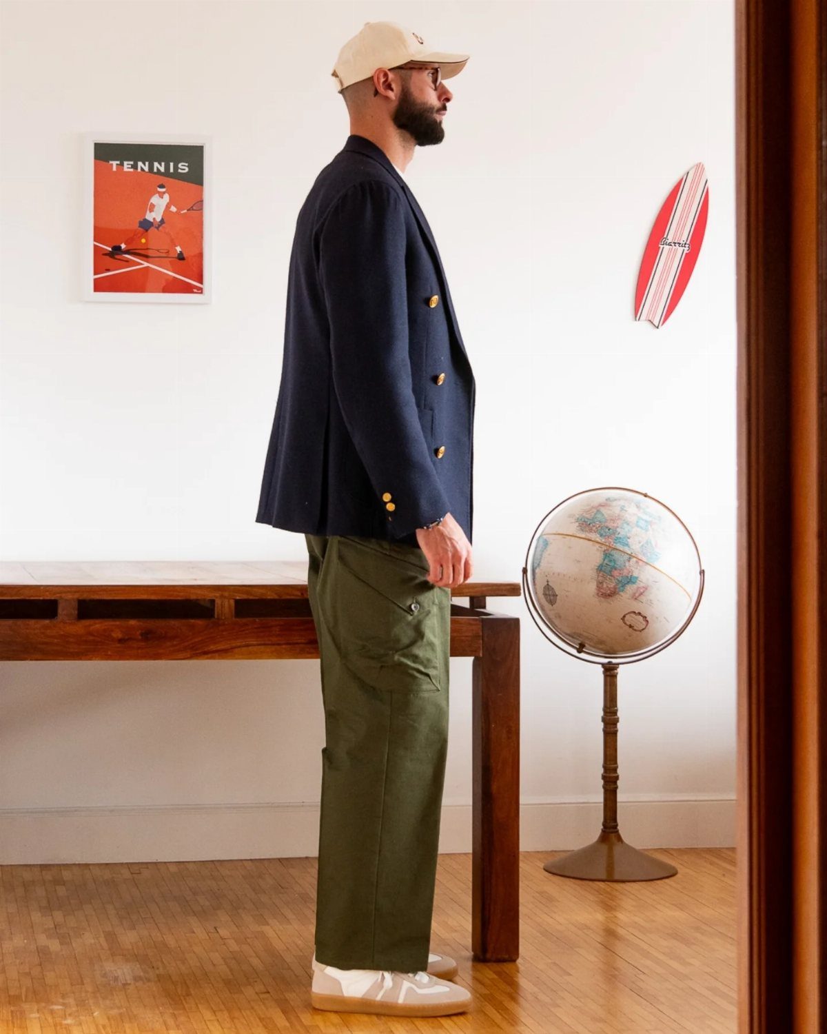 A man standing in profile wearing a navy blazer and olive green cargo pants.