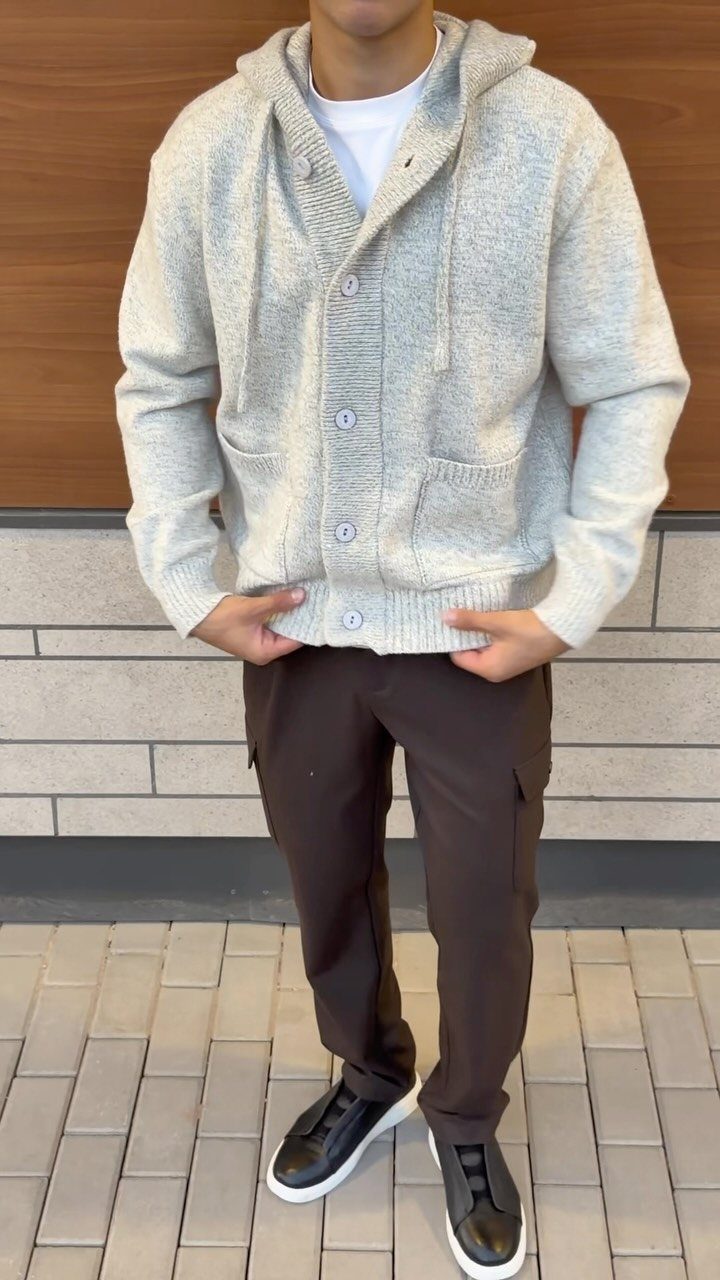 A person wearing a light grey hooded cardigan and brown cargo pants with black sneakers.