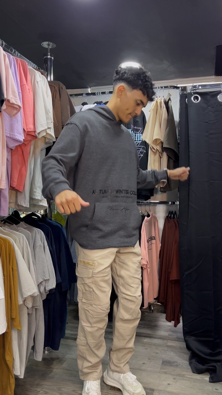 A young man wearing a grey hoodie and beige cargo pants in a clothing store.
