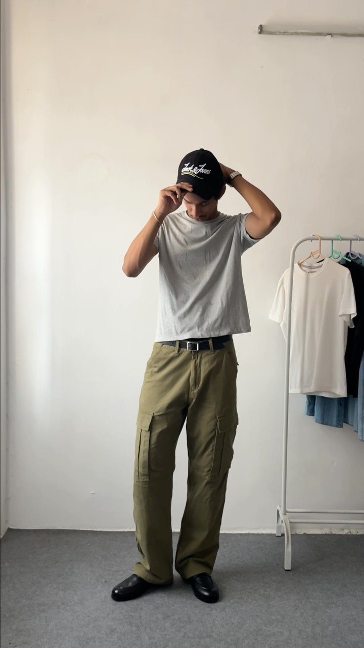 A person wearing olive green cargo pants, a grey t-shirt, and a black cap.