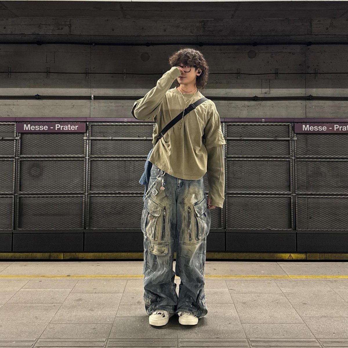 A person wearing baggy distressed denim cargo pants and an olive long-sleeve shirt in a subway station.
