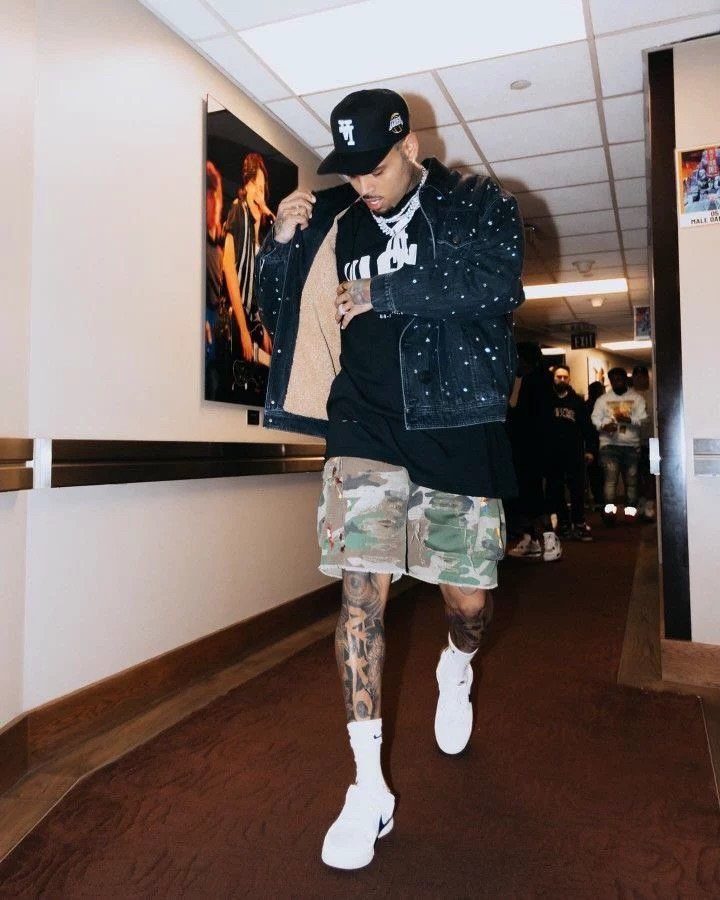A man walking in a hallway wearing a denim jacket and camouflage cargo shorts.