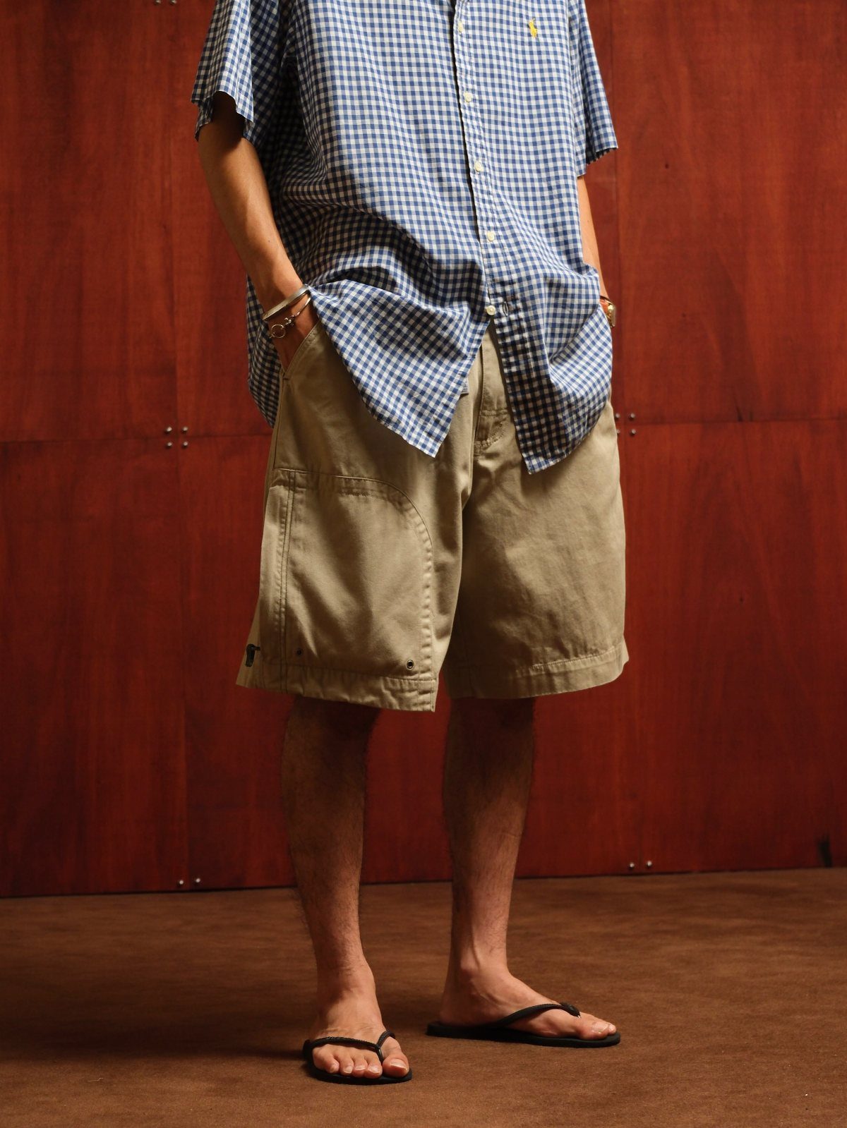 A person wearing a blue gingham shirt and khaki cargo shorts with black flip-flops.