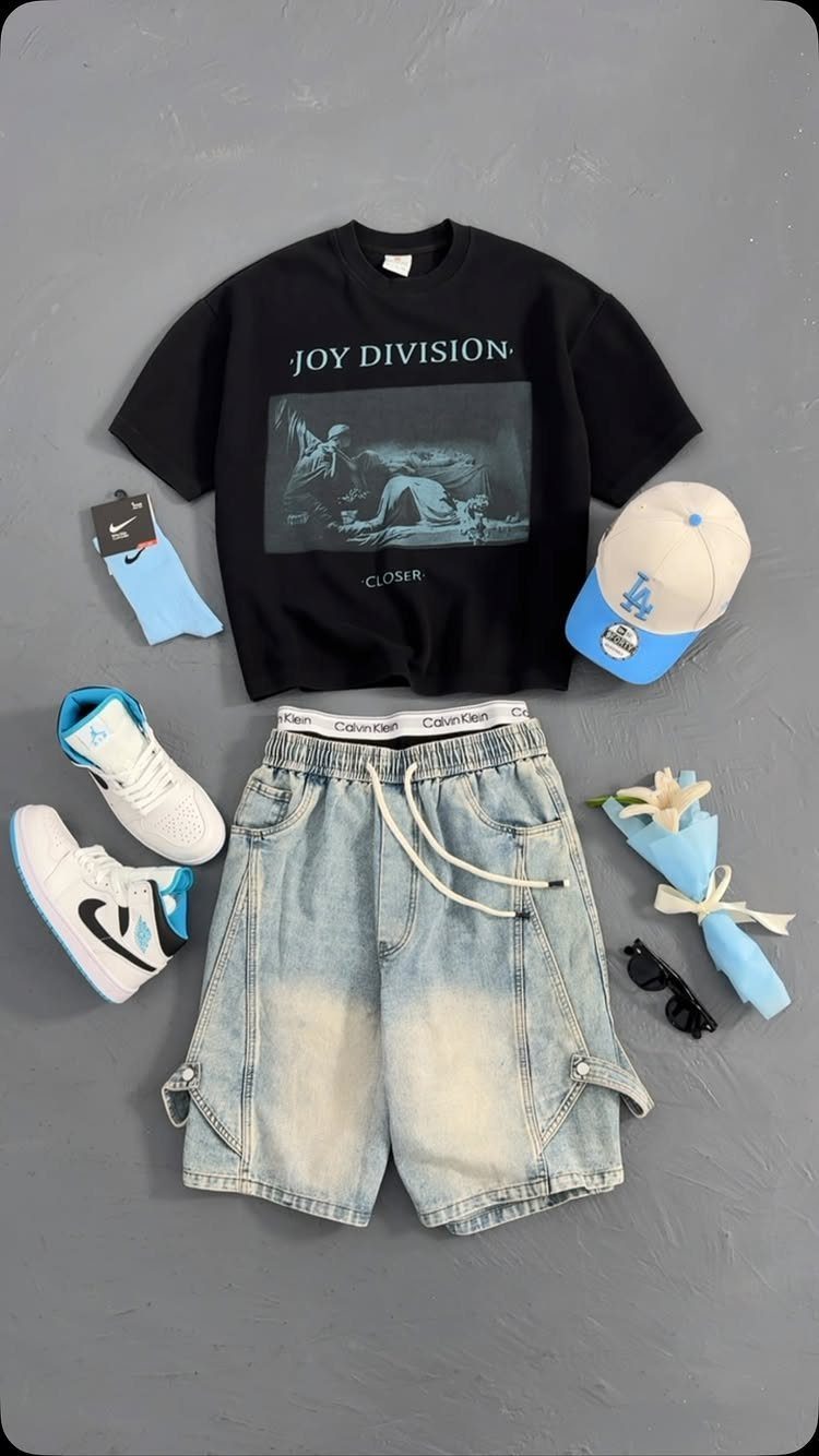 Flat lay of a black graphic t-shirt, light blue denim cargo shorts, and blue and white sneakers.