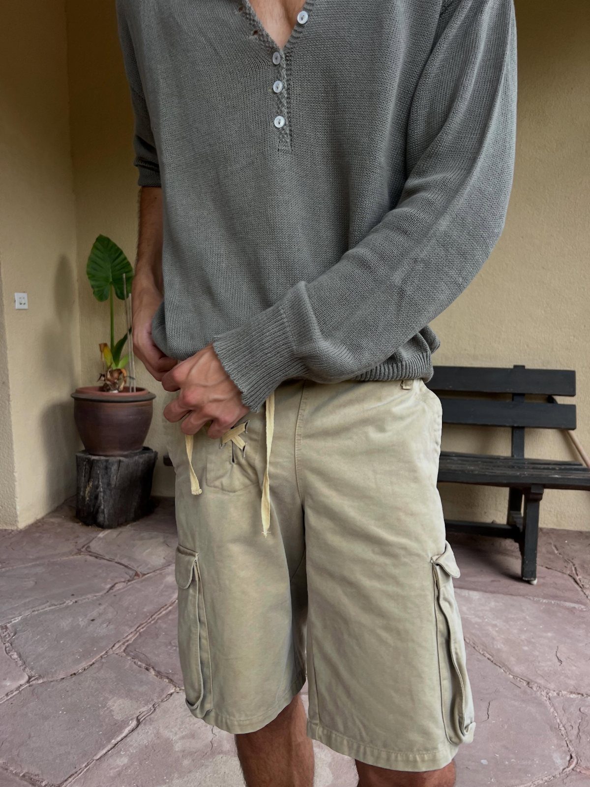 A person wearing a grey textured henley shirt and beige cargo shorts standing outdoors.