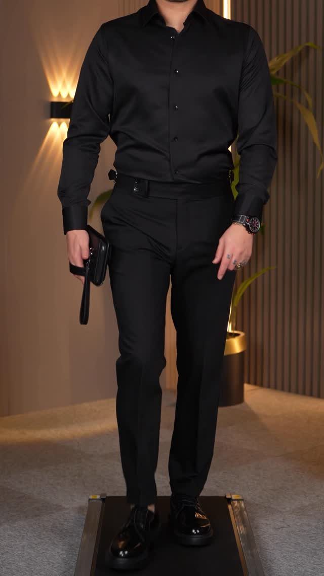 Man wearing a black long-sleeved button-down shirt and matching black tailored trousers.