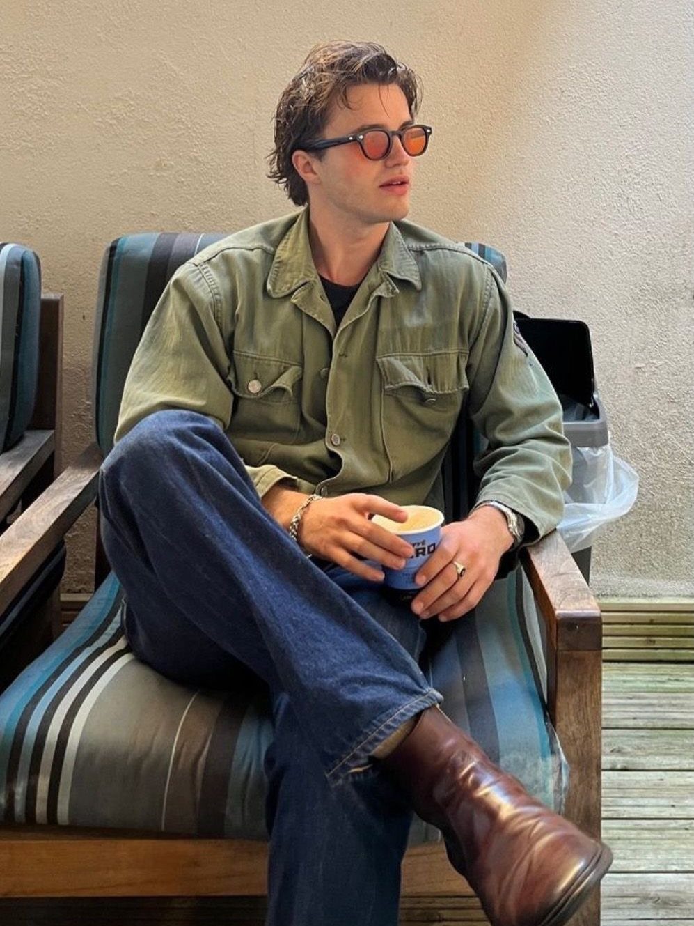 Man sitting in a chair wearing an olive green utility overshirt and blue jeans.