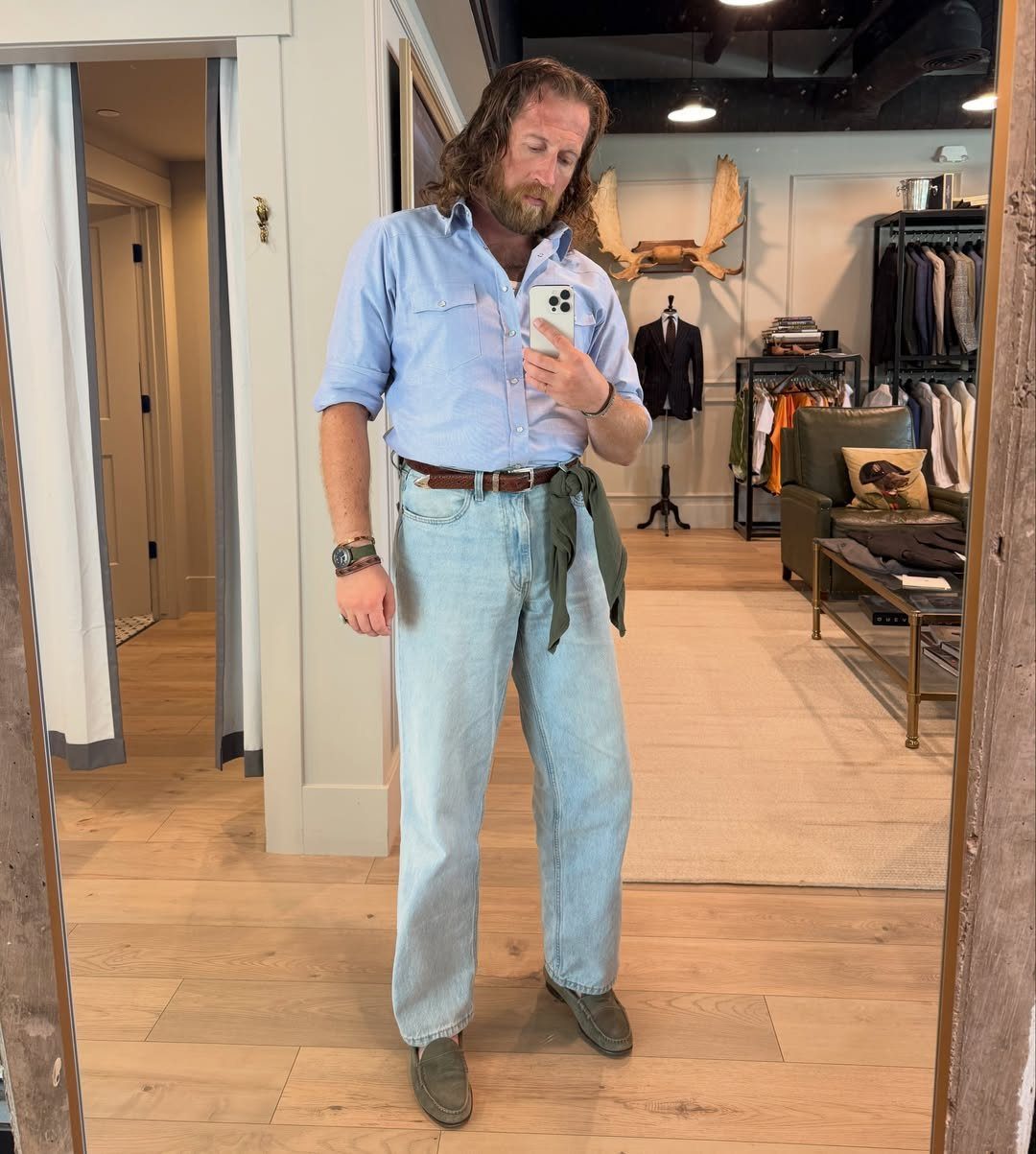 A man posing in a mirror wearing a light blue shirt and light-wash blue jeans.