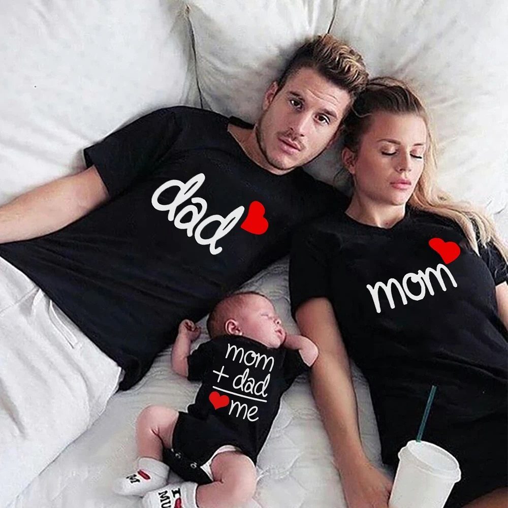A family of three lying on a white bed wearing matching black graphic t-shirts.