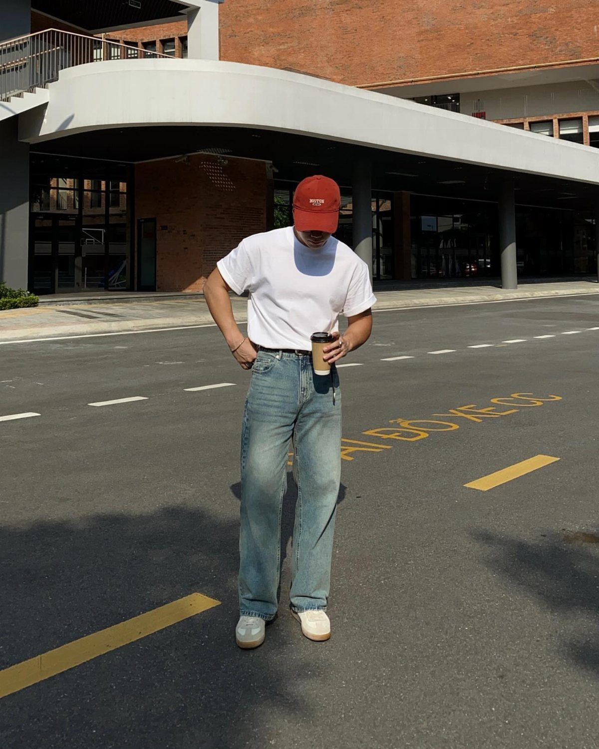 Man wearing a white t-shirt tucked into light blue jeans and a red cap.