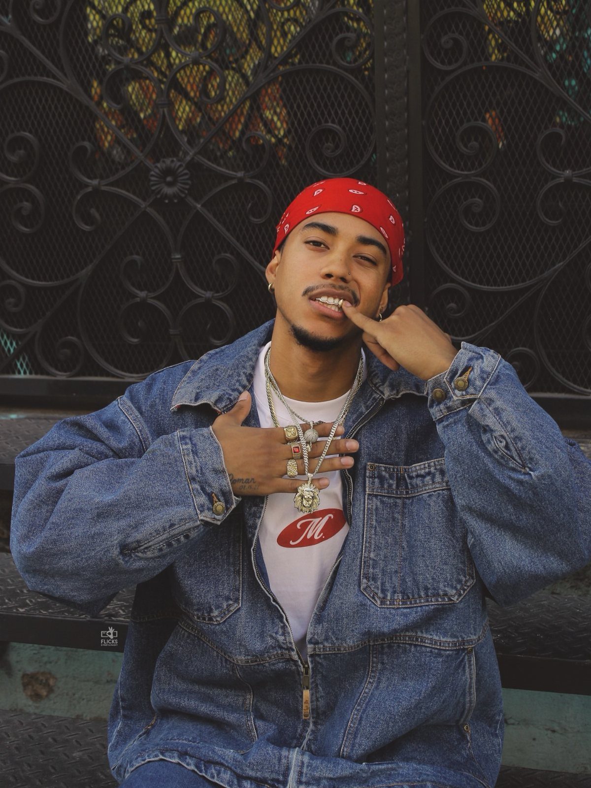 A young man in a red bandana and oversized denim jacket posing outdoors.
