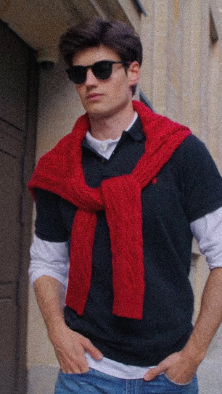 Man in black polo shirt and red sweater draped over his shoulders wearing sunglasses.